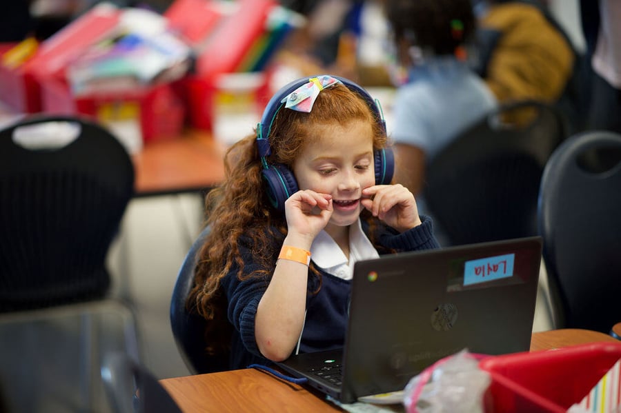 young girl wearing headphones and looking at a laptop