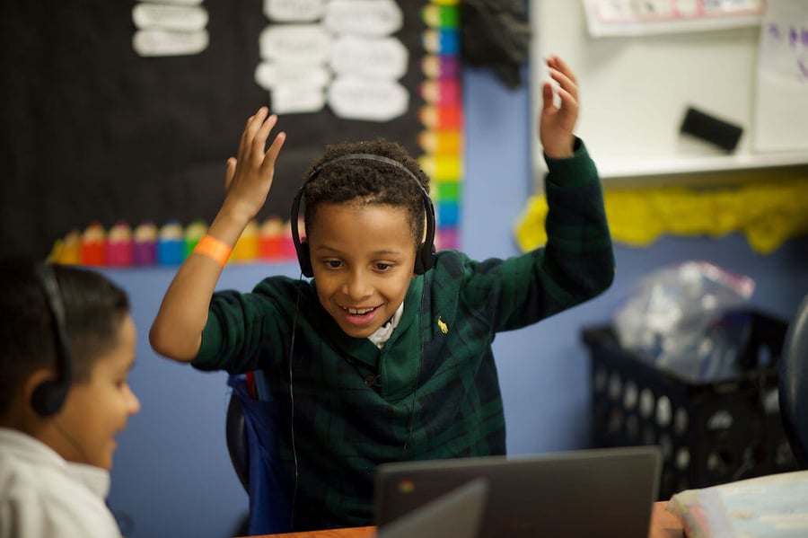 a young boy wearing headphones and looking at a laptop screen with his hands in the air