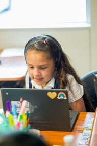 young girl wearing headphones and looking at a laptop